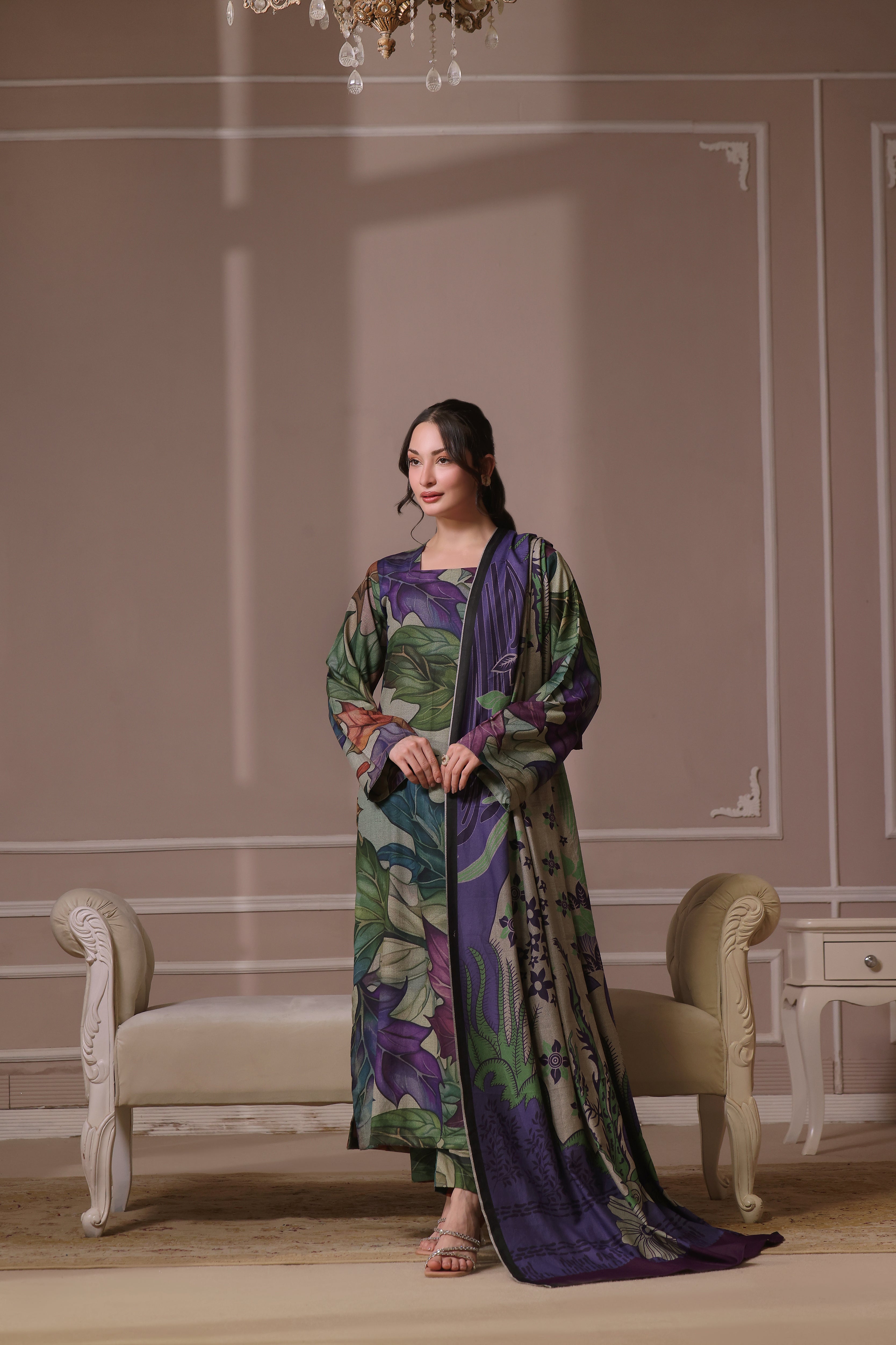A woman standing in a beautifully decorated room wearing a traditional, digitally printed shawl with a floral design in shades of purple and blue.